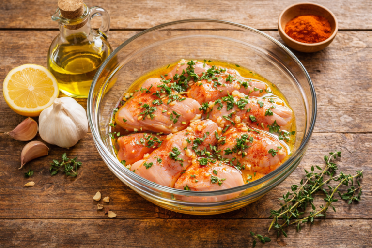 Poulet en train de mariner dans un bol en verre avec huile d'olive, citron, ail et herbes